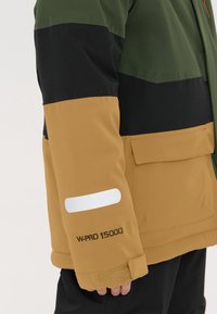 Jas met een kleurblokkenontwerp in groen, zwart en beige, met een witte accent op de mouw en het label "W-PRO 15000".