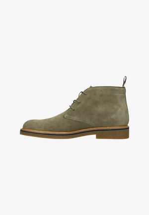 Bottine homme en daim vert olive avec semelle beige, lacets à l'avant et languette à l'arrière, vue de profil sur fond blanc.