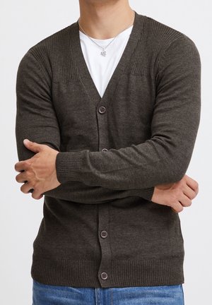 Mörkbrun kofta med V-ringning, ribbade axeldetaljer och fem knappar. Tillverkad av mjukt material, med åtsittande ärmslut och midja.