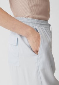 Pantaloni azzurri chiari con vita elastica, dotati di tasche laterali e una tasca con pattina sul retro. Tessuto morbido con una texture liscia.