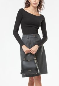 Bolso de mano de cuero negro con herrajes dorados, de forma cuadrada, con el logo "V-73" en la parte frontal y una correa corta; combinado con una blusa negra de manga larga y una falda a rayas.