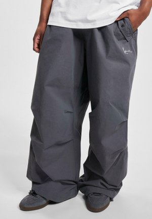 Baggy, gray trousers made of a lightweight fabric, featuring a buttoned pocket and a subtle embroidered logo on the front.