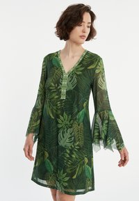 Grün gemustertes Kleid mit Blattdesign, V-Ausschnitt, langen ausgestellt Ärmeln und einer strukturierten Borte entlang des Ausschnitts. Hergestellt aus einem leichten, durchsichtigen Material.