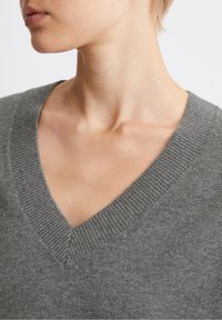 Pull gris à col en V avec un col côtelé et une texture douce, avec une coupe ajustée mise en avant autour du col et de la partie supérieure de la poitrine.