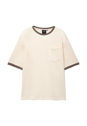 T-shirt à manches courtes de couleur crème avec un tissu texturé, encolure et bords de manches en côte marron, avec une petite poche sur la poitrine.