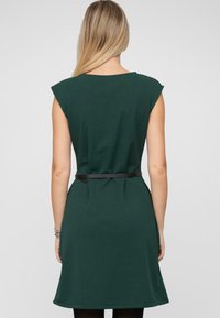 Grünes ärmelloses Kleid mit tailliertem Oberteil, schwingendem Rock und schwarzem Gürtel in der Taille. Glattes Material mit subtiler Textur, knielang.