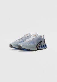 Grey textured athletic shoes with a mesh upper, featuring a padded collar, lacing system, and a distinctive sole with blue accents.