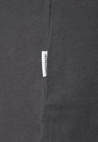 Mørkegrå sweatshirt-stoff med ribbet tekstur. Har en liten hvit tagg merket "JACK & JONES" på sidesømmen.