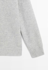 Grå ribbad tröja med en mjuk textur, långa ärmar och en figursydd nederkant. Designen betonar vertikala linjer genom hela tyget.