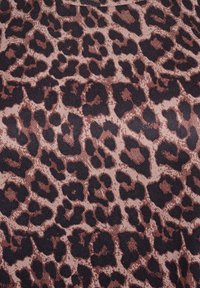 Close-up af brun og sort leopardmønsterstof med uregelmæssige, organiske pletter på beige baggrund.