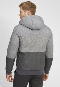 Hooded jacket with a textured grey fabric featuring three horizontal color blocks: light grey, medium grey, and dark grey at the bottom.