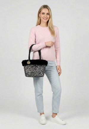 Woman in pink sweater and light jeans holding black sequined handbag with braided handles, standing against plain background.