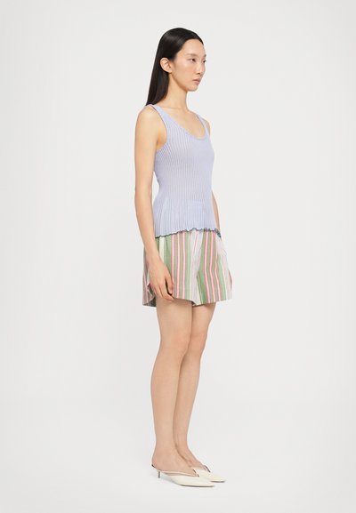 Top en maille violet clair associé à une mini jupe plissée rayée de couleurs verte, rose et blanche. Le mannequin porte des mules de couleur claire.