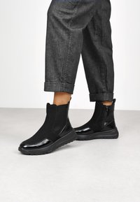 Bottines noires avec un design épuré, présentant une finition lisse et une semelle en caoutchouc. Des accents texturés améliorent leur apparence moderne.
