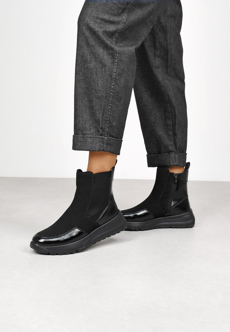 Bottines noires avec un design épuré, présentant une finition lisse et une semelle en caoutchouc. Des accents texturés améliorent leur apparence moderne.