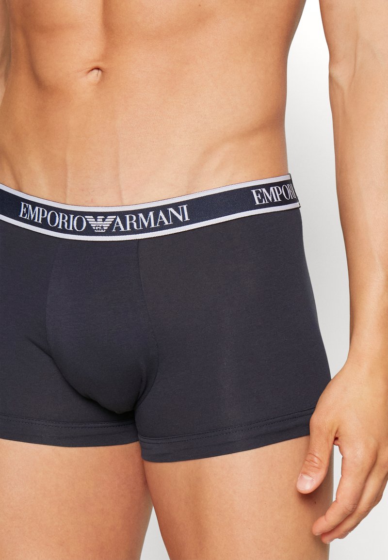 Boxers gris foncé avec une texture douce, présentant une ceinture contrastante étiquetée « EMPORIO ARMANI » en blanc et bleu marine.