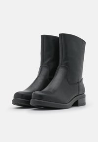 Bottines en cuir noir avec une pointe ronde, une texture lisse, et un panneau latéral élastique. Le talon bloc mesure environ 2 cm de hauteur.