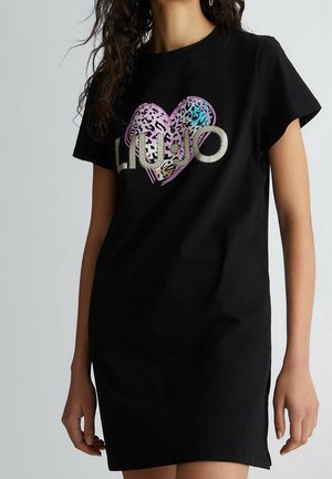 Woman wearing a black short-sleeve dress with a colorful leopard-print heart and "Liu Jo" text on the chest.