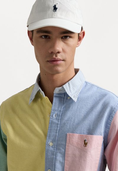 Camisa de botão multicolorida com secções em amarelo, azul, rosa e verde, com um colarinho riscado. Inclui logótipo bordado no peito.