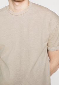 Béžové bavlněné tričko s kulatým výstřihem a krátkými rukávy, které má jemnou, hladkou strukturu a uvolněný střih.