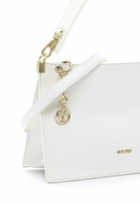 Sac à main en cuir blanc texturé avec des accessoires dorés, une bandoulière amovible et un charm circulaire doré suspendu près du coin supérieur.