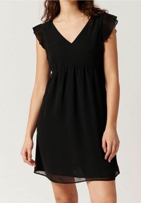 Svart klänning med V-ringning, veckade kappryggar och empiremidja. Tillverkad av lätt material, den har en flödande silhuett.