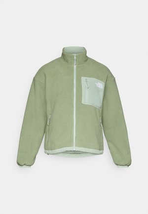 Fleecejakke i lys grønn, med høy krage, full glidelås foran og en brystlomme med kontrasterende stoff. Elastisk mansjetter og hem.