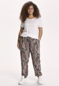 Weißes V-Ausschnitt-T-Shirt kombiniert mit lockeren, gemusterten Hosen in dunklen Tönen, die Paisley-Muster und einen Kordelzugbund aufweisen.