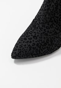 Botte noire à bout pointu avec un motif léopard texturé, en tissu à finition douce. Semelle lisse et design élégant.