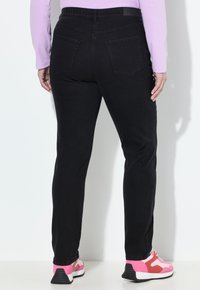 Jeans negros ajustados con una cinturilla elástica y dos bolsillos traseros. Combinados con zapatillas rosas y blancas. Tejido liso con textura mínima.