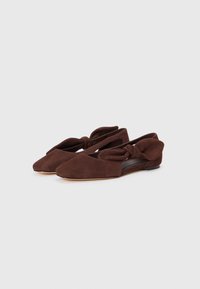 Brown suede flats with a pointed toe, side cutouts, and a knotted bow detail at the heel, featuring a smooth leather insole.