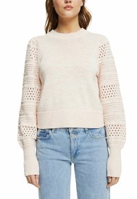 Pull court rose clair avec un col côtelé et des manches en maille texturée présentant des rayures horizontales et des motifs ajourés.