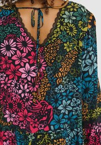 Gros plan sur une robe imprimée florale colorée, manches longues, encolure bordée de dentelle et lien à nouer avec perles en bois dans le dos.