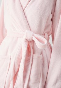 Pink bathrobe made of soft, plush material. Features a wrap design with a tied waist belt and two front pockets.