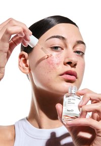 Bottiglia di vetro trasparente con un'etichetta bianca che riporta la scritta "PURE PEEL AHA SOLUTION". Siringa a goccia che eroga il liquido sulla pelle con imperfezioni visibili.
