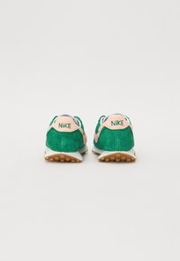 Žalios zomšos sportbačiai su rožiniais akcentais, turintys baltą ir šviesiai mėlyną tarpmisolį bei rudą gumos pado apvalkalą. „NIKE“ logotipas ant kulno.