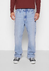 Vaaleansiniset rentomalliset farkut, joissa on klassinen viiden taskun muotoilu ja hienovarainen kulutus. Yhdistetty mustiin tennareihin.