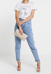 Bílé tričko s černým liniovým motivem, světle modré džínové kalhoty s vysokým pasem, tělové psaníčko a béžové sandály na podpatku.