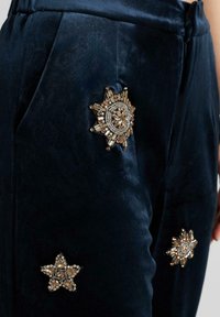 Pantalones de terciopelo azul marino con embellishments de sol y estrellas con tachuelas doradas en los bolsillos, que presentan una textura suave y un diseño de corte relajado.