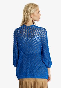 Zila mežģīņu topiņš ar trim ceturtdaļām piedurknēm, kuram ir dimanta raksts un brīvs piegriezums. Aizmugurē atklājas teksturēts, atvērts dizains.