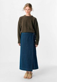 Brun, struktureret trøje parret med en lang, blå denimnederdel med en sidelukning. Modellen bærer beige sandaler; minimalistisk design, neutrale farver.