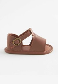 Brun lädersandal med tåröppning och korsbanddesign. Har en rundad bakdel och spänne på sidan. Slät textur.