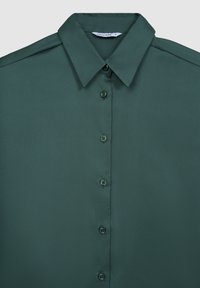 Camicia color verde scuro con colletto e una texture liscia, dotata di sei bottoni sul davanti e dettagli sottili sulle spalle.