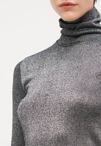 Pull en col roulé argent métallique avec un design élégant et près du corps, en tissu doux et texturé, avec un effet de brillance subtil.