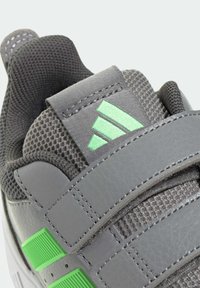 Zapatilla gris con parte superior de cuero texturizado, lengüeta de malla, detalles verdes y tres correas ajustables para un ajuste seguro.