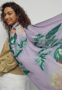 Gaisma purpursarkana šalle ar spilgtiem ziedu rakstiem zaļā un oranžā krāsā. Audums glīti karājas, piešķirot apģērbam mīkstumu.