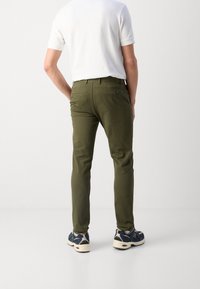 Heren chinos in olijfgroen van een katoenmix, met een slim fit, achterzakken, gedragen met marineblauwe en crèmekleurige sneakers.