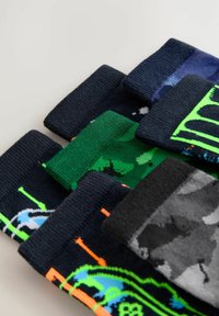 Cinque paia di calzini di vari colori, con fantasie e trame: nero, verde, blu e dettagli neon con design giocosi.