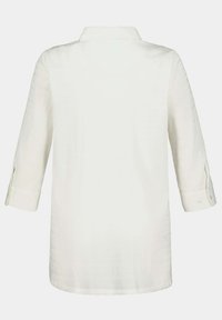 Blusa blanca con cuello, mangas largas enrolladas hasta tres cuartos y una tela texturizada. Botones en los puños y un dobladillo recto.