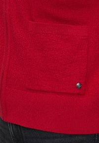 Czerwony sweter o fakturze z przodu z kieszenią i srebrnym zatrzaskiem oraz ribbowanym wykończeniem.